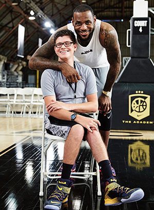 LeBron James putting his arm around the shoulder of a smiling teen, sitting in a chair