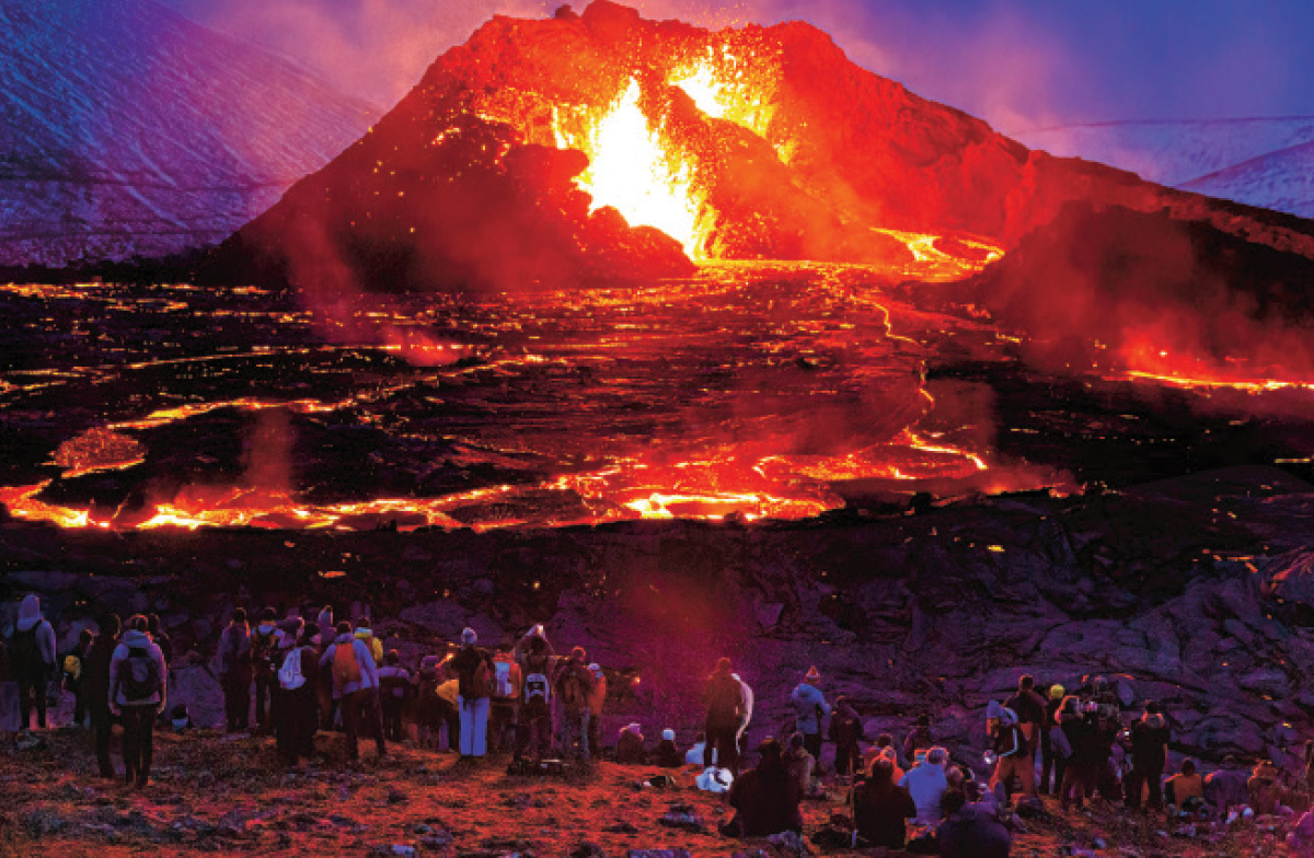 Photo of scientists gathered around a volcano spewing lava