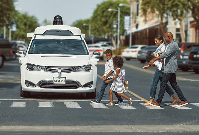 A family of four crossing the road with car with a camera on it in the background