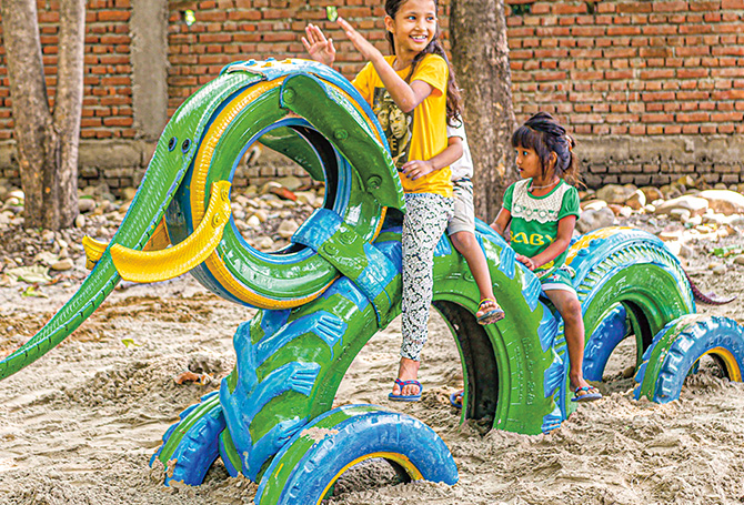 Children playing on a colorful elephant made from tires