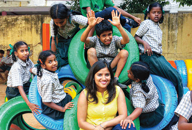 Students sitting on tires surrounding a smiling adult